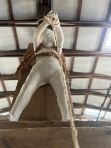 Installation mit weißer Skulptur (Boy) an Treibholz festgebunden (trägt das Holz wie einen Tornister). 